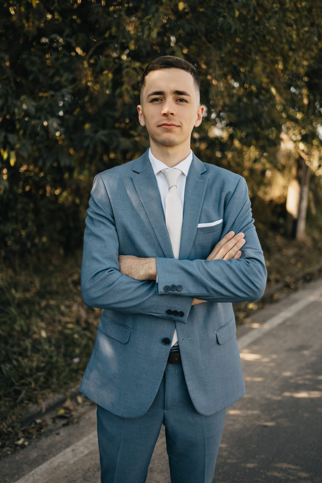 João Pedro de terno azul e gravata clara, de braços cruzados, olhando para a câmera